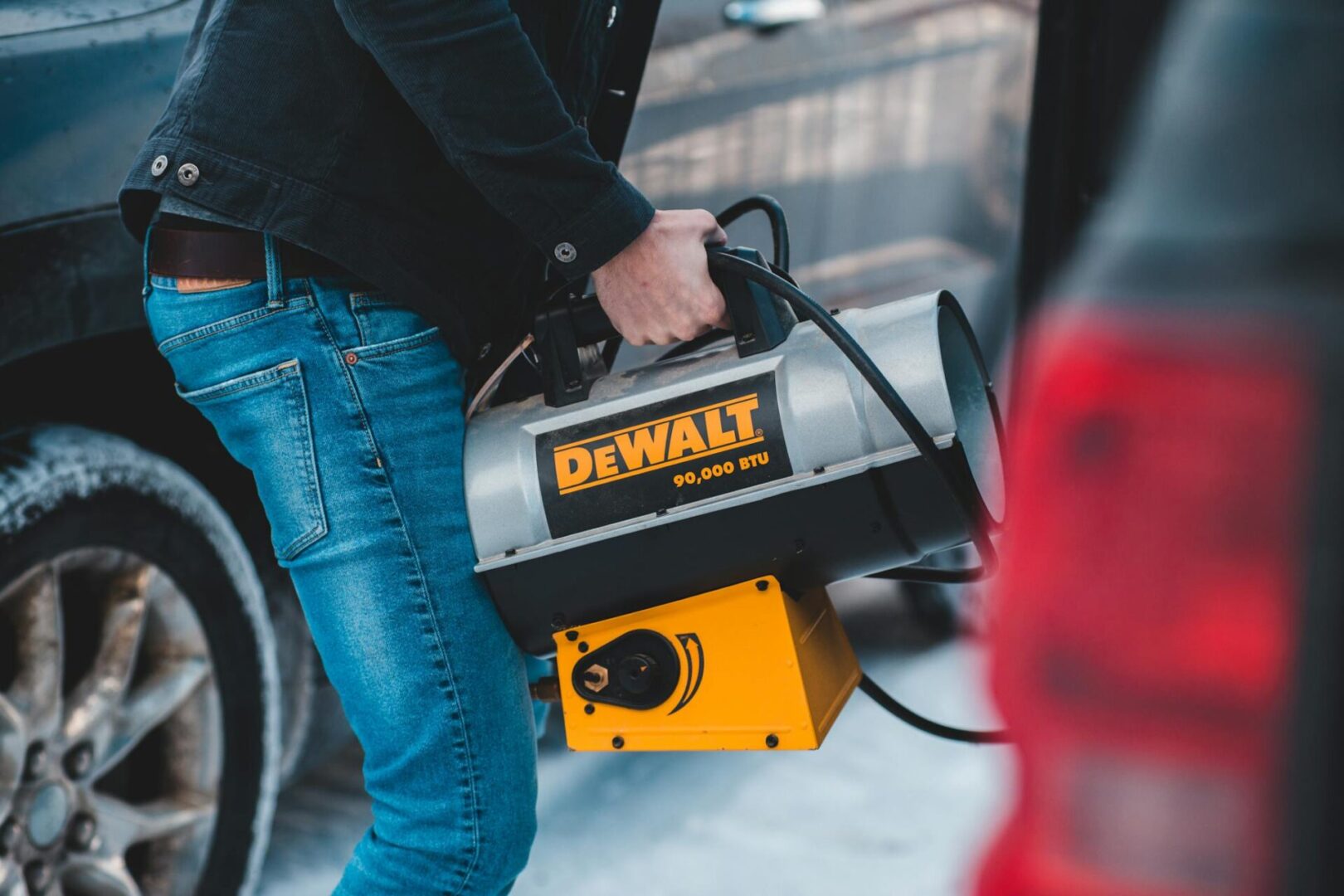 Faceless man carrying portable heater standing near cars on street